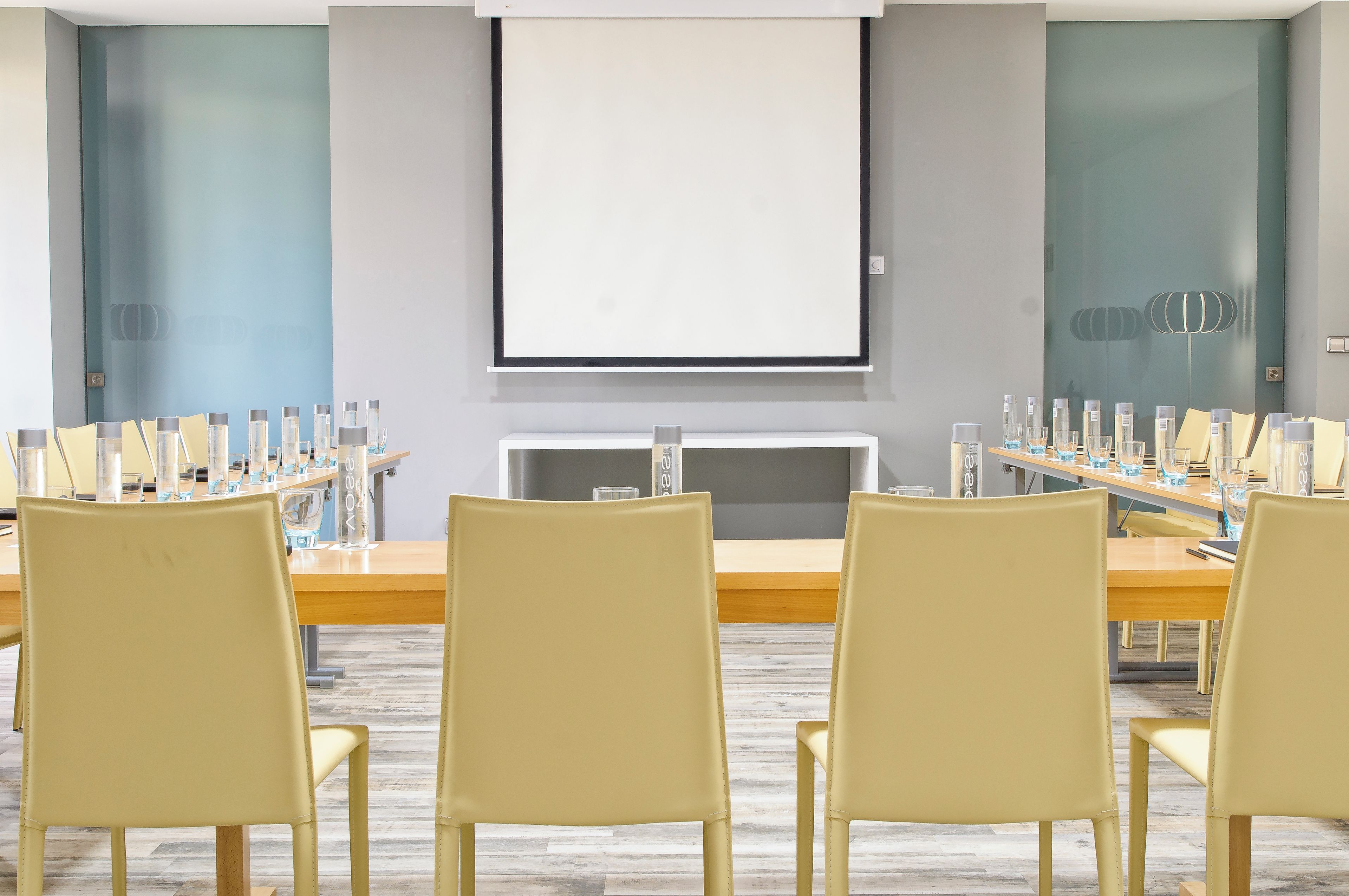 A conference room with a long table, multiple chairs, and a projector screen.