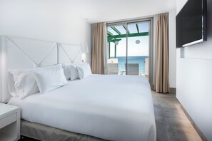 A hotel room with a large bed, a television mounted on the wall, and a view of the sea through the window. - Barceló Teguise Beach - Adults only (Teguise)