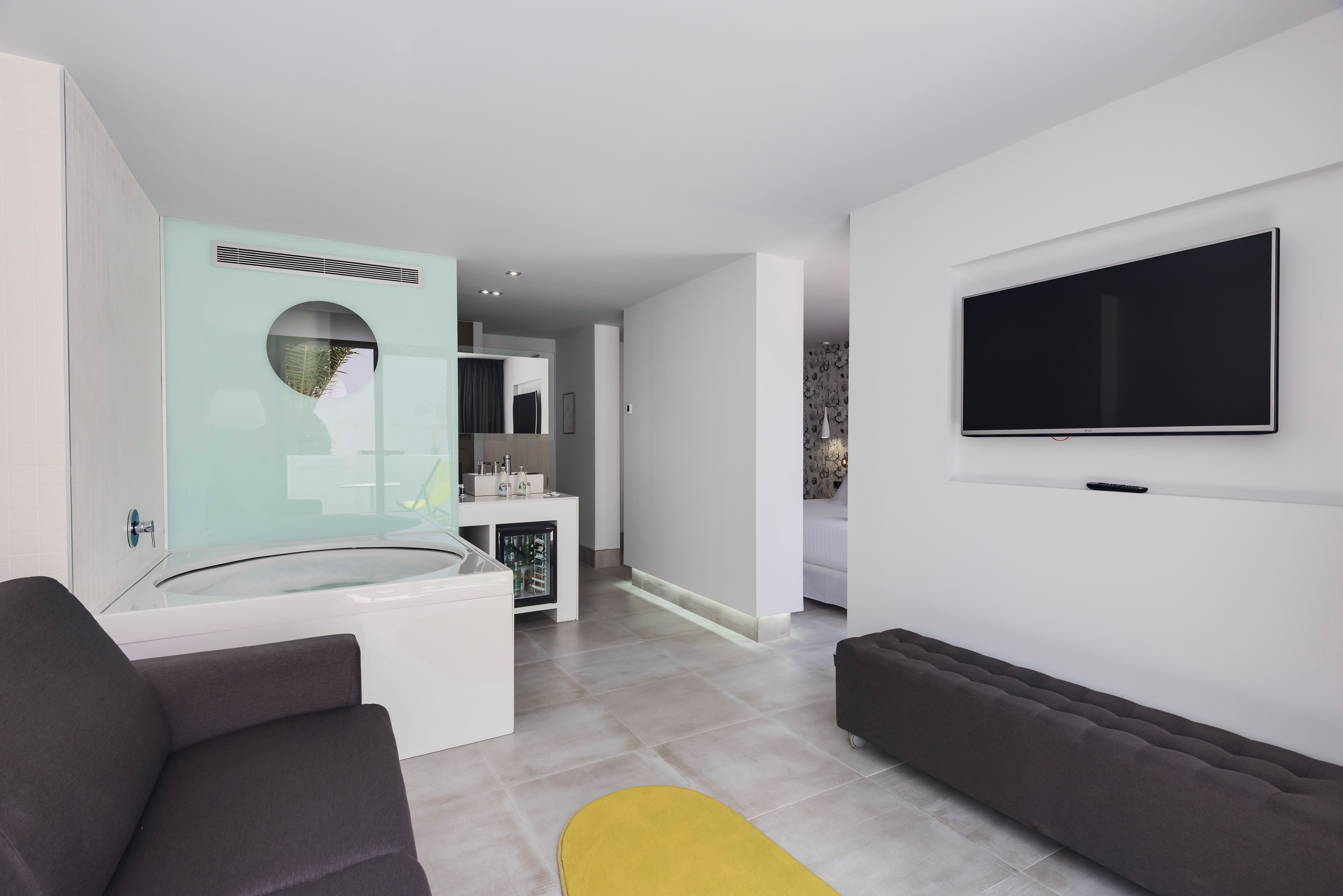 Een moderne woonkamer met een flatscreen televisie, een zithoek met glazen wanden en een kleine koelkast.