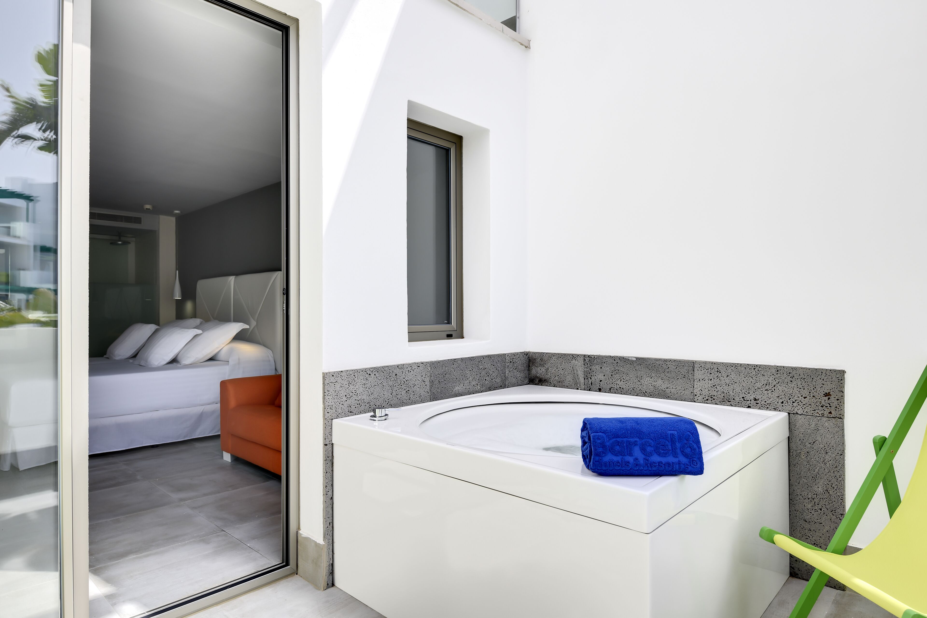 A modern bathroom with a white bathtub, a small window, and a green chair.