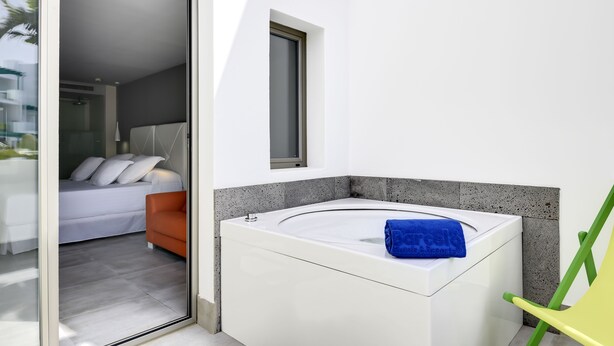 A modern bathroom with a white bathtub, a small window, and a green chair. - Barceló Teguise Beach - Adults only (Teguise)