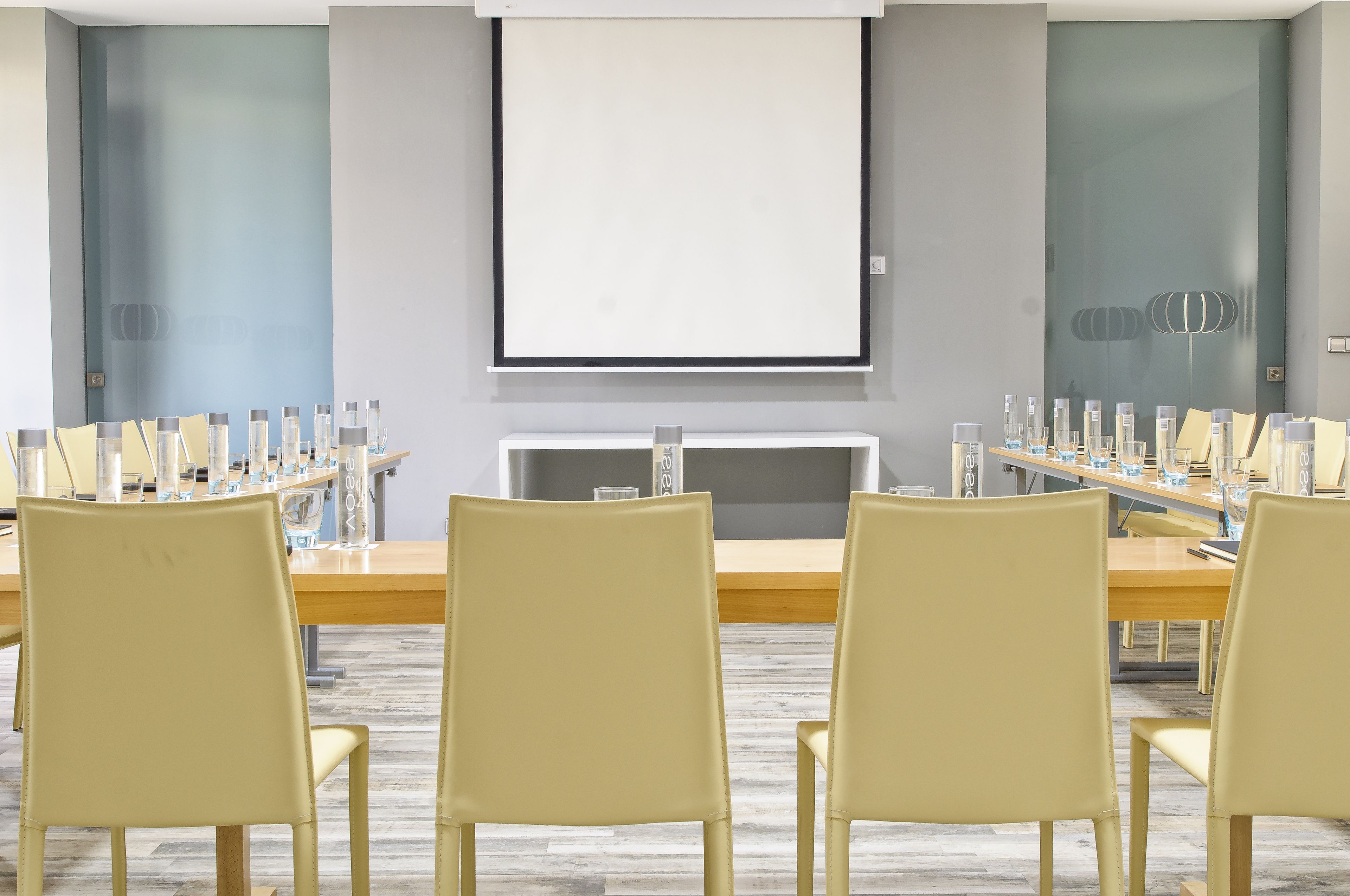 A conference room with a long table, multiple chairs, and a projector screen.