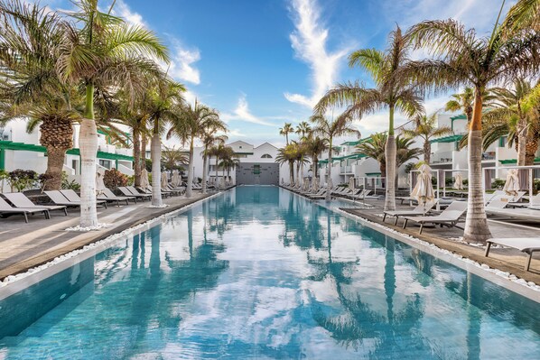 A pool with lounge chairs and palm trees, surrounded by buildings. - Barceló Teguise Beach - Adults only (Teguise)