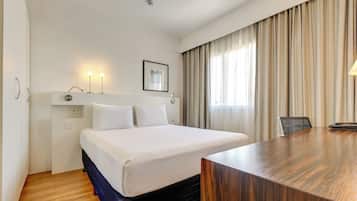 Habitación de hotel con una cama grande, un escritorio, una silla, un cuadro en la pared y una ventana con cortinas.