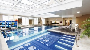 Una amplia piscina interior con agua cristalina y azul, rodeada por una solana con baldosas y un techo de cristal.