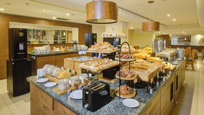 Un bufé con diversas opciones de comida, una máquina de café y un refrigerador.