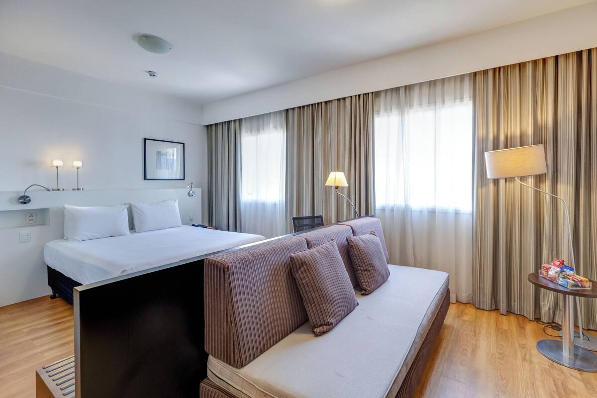 A hotel room with a bed, a sofa, a desk, and a lamp.