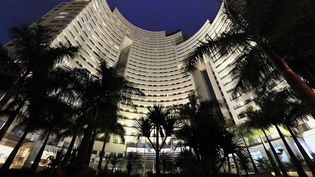 Un hotel moderno de gran altura con fachada curva, varios pisos y palmeras en primer plano.