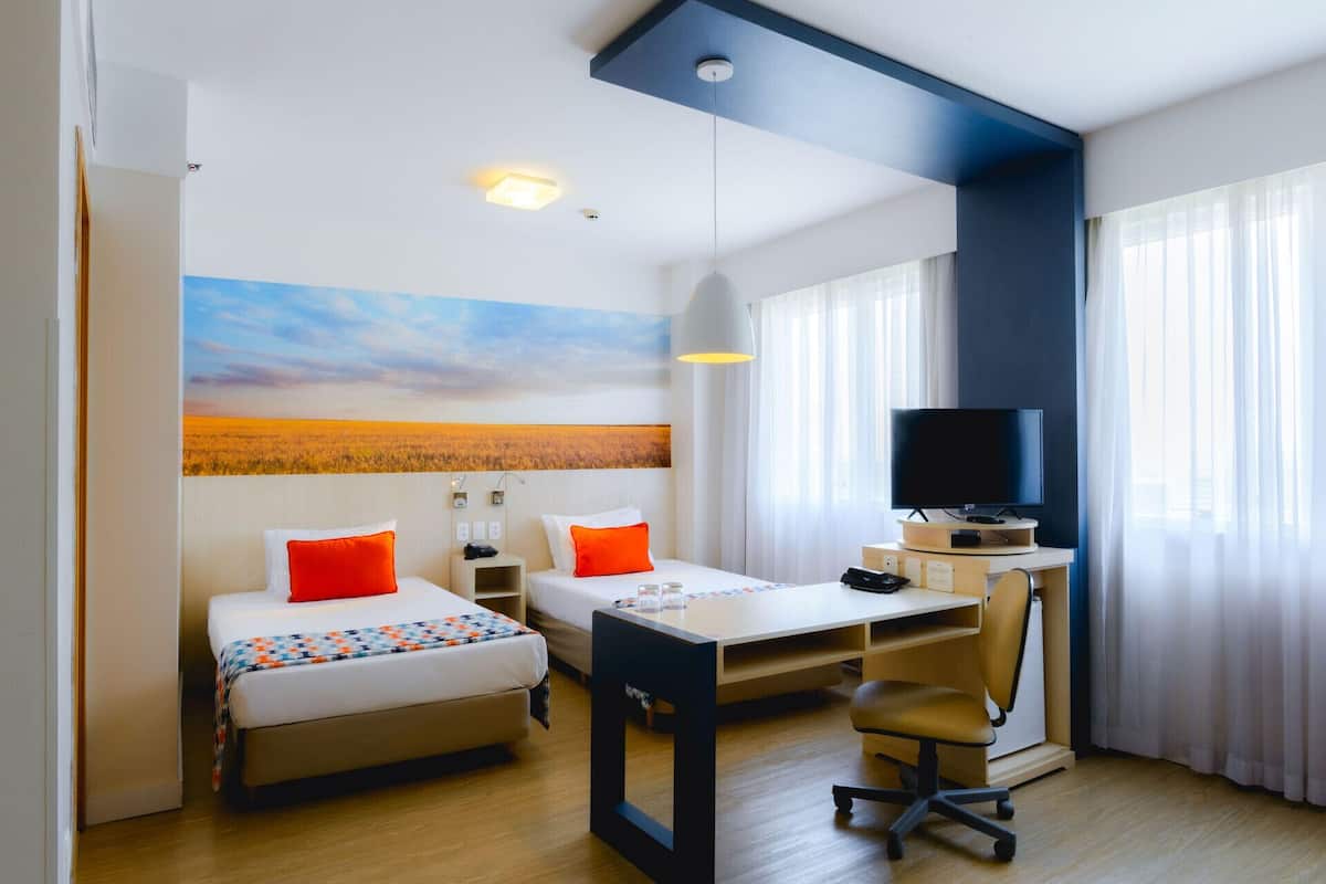 A hotel room with two beds, a desk, a television, and a large window.