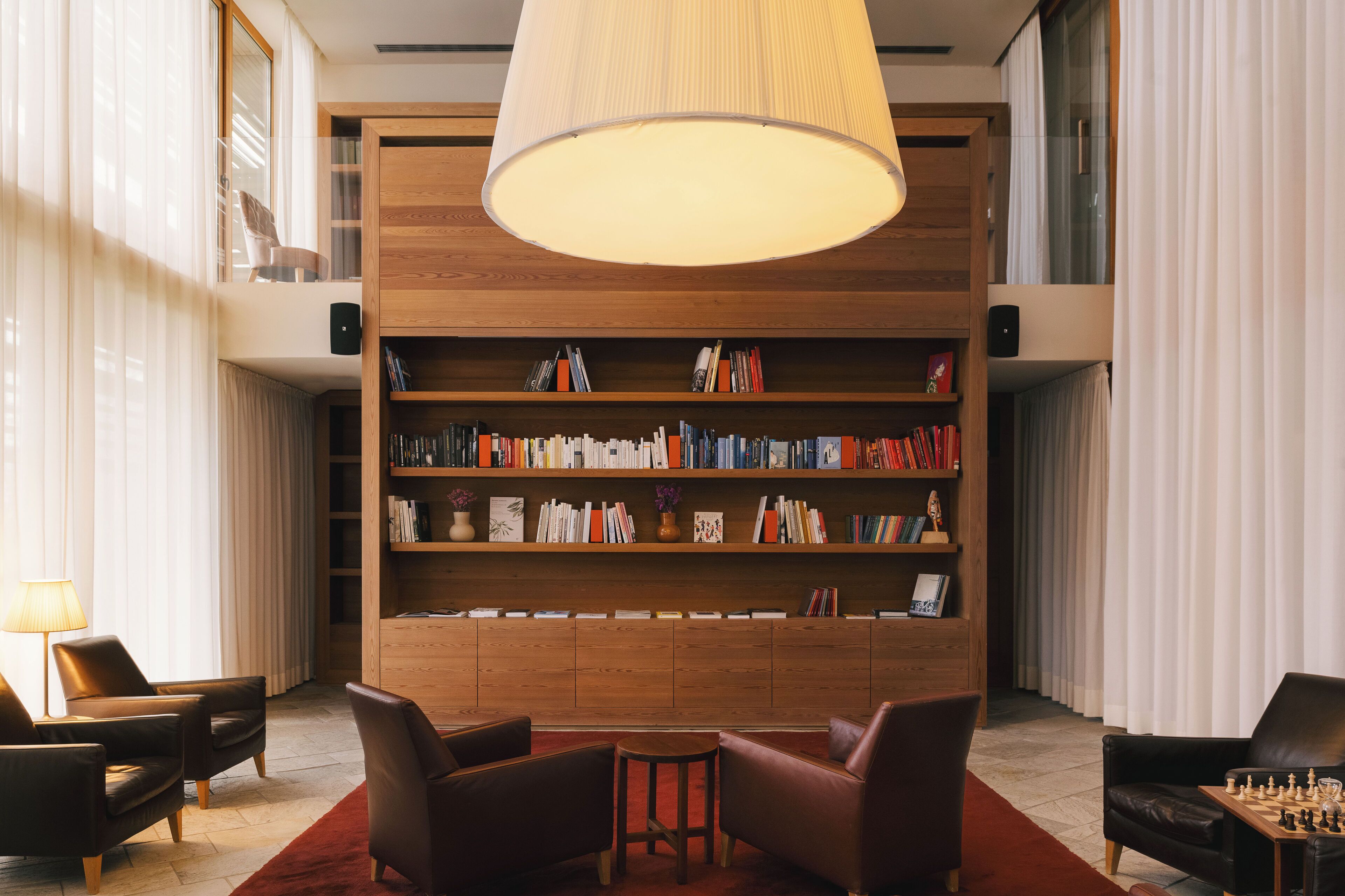 A modern library with leather chairs, a wooden bookshelf, and a large hanging light fixture.