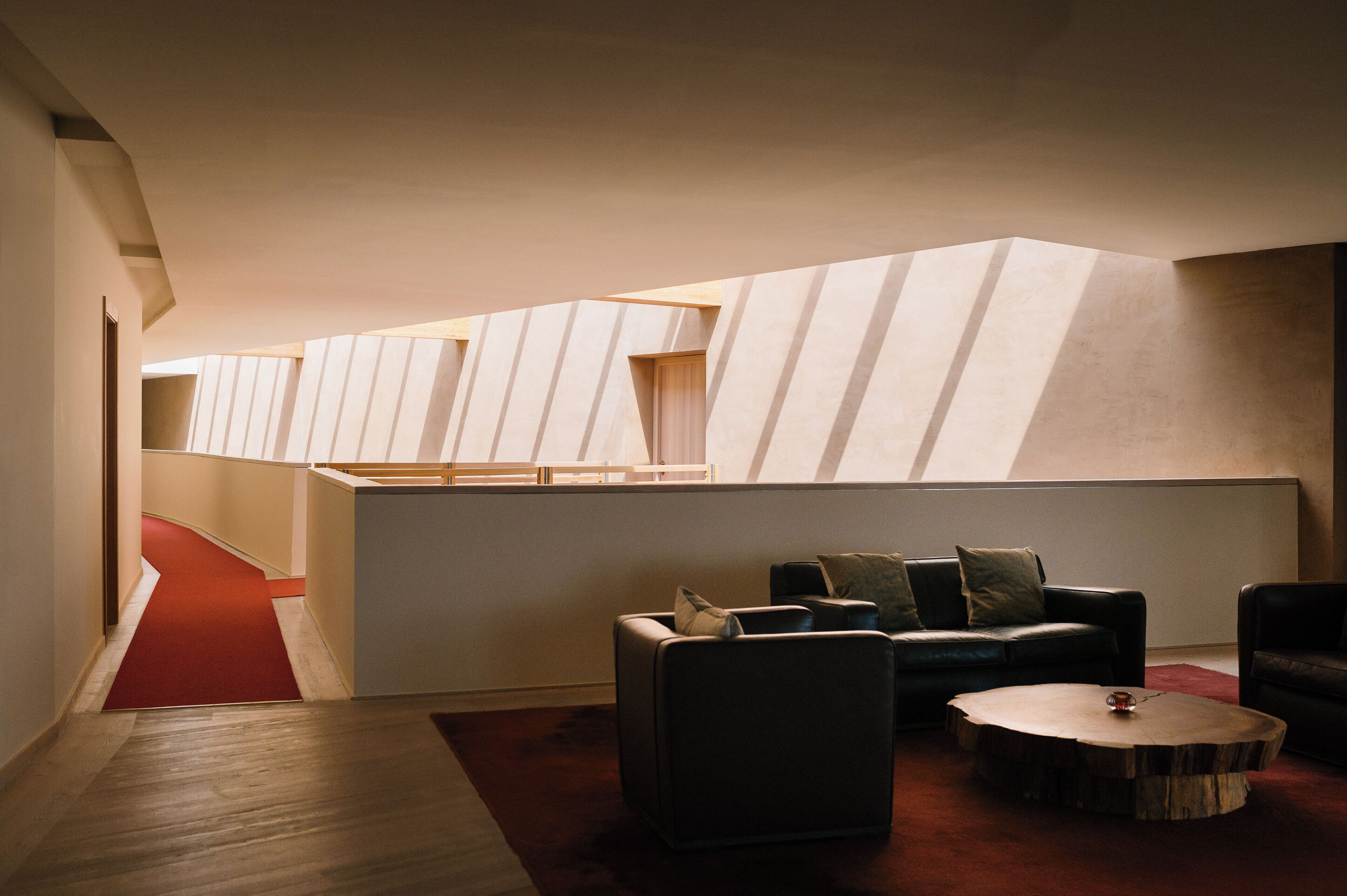 A modern interior with a sloped ceiling, a red carpeted hallway, and a seating area with a round coffee table.