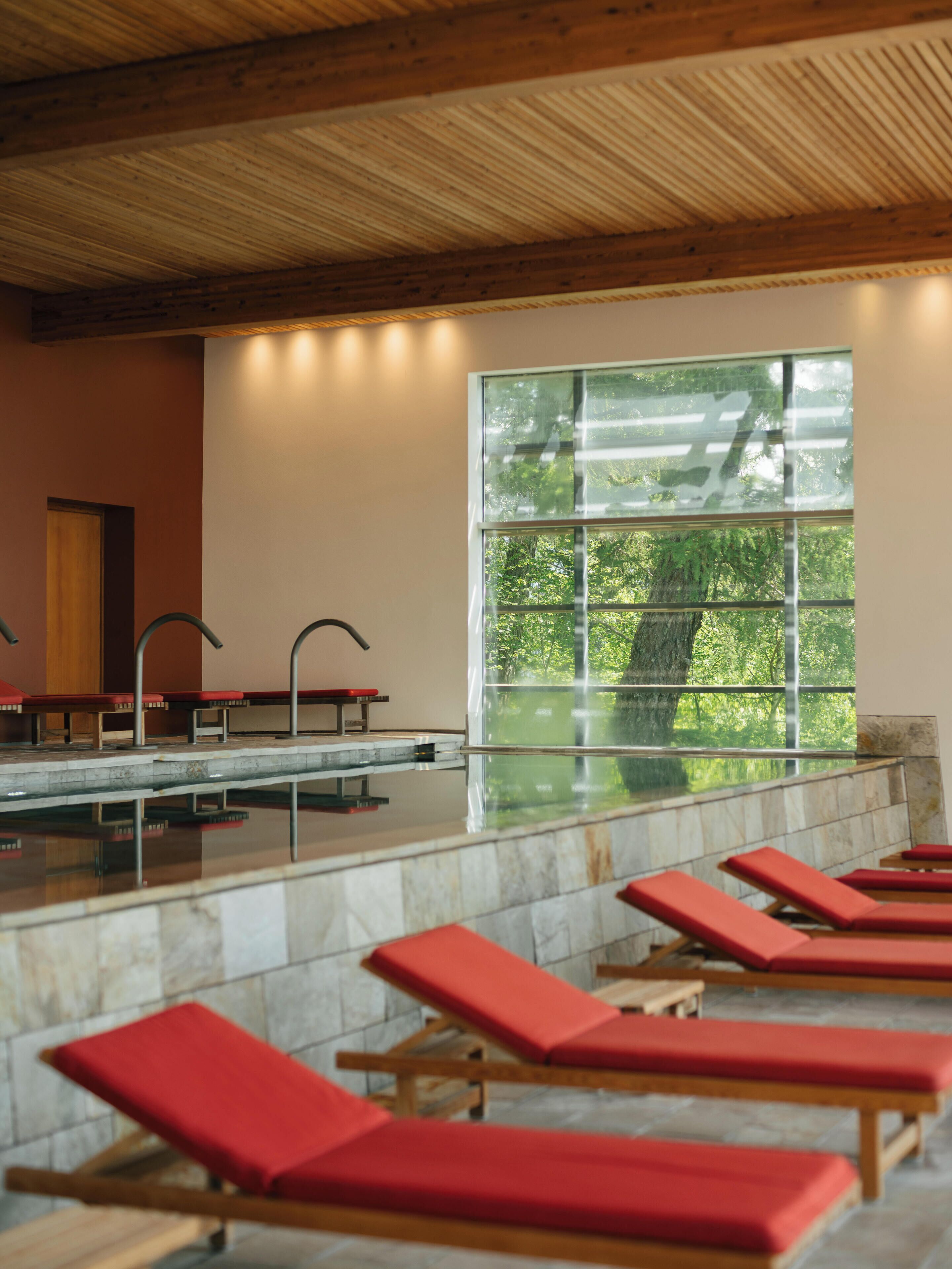A spa area with red lounge chairs, a marble pool, and a large window with a view of trees.