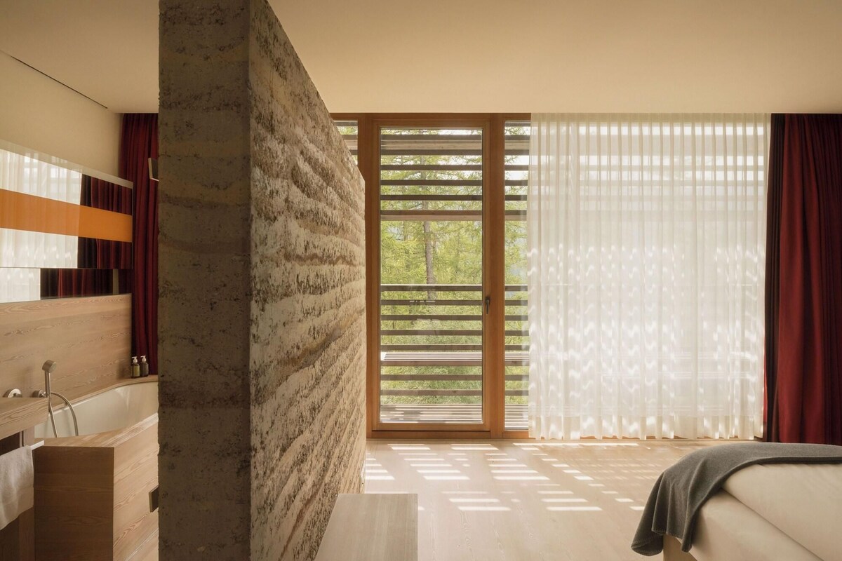 A modern bathroom with a wooden vanity, a bathtub, and a large window with blinds.