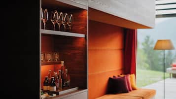 Ein modernes Interieur mit einer Holzkabine, in der Weingläser und Flaschen aufbewahrt werden, einer Couch mit Kissen und Blick auf Grünflächen.