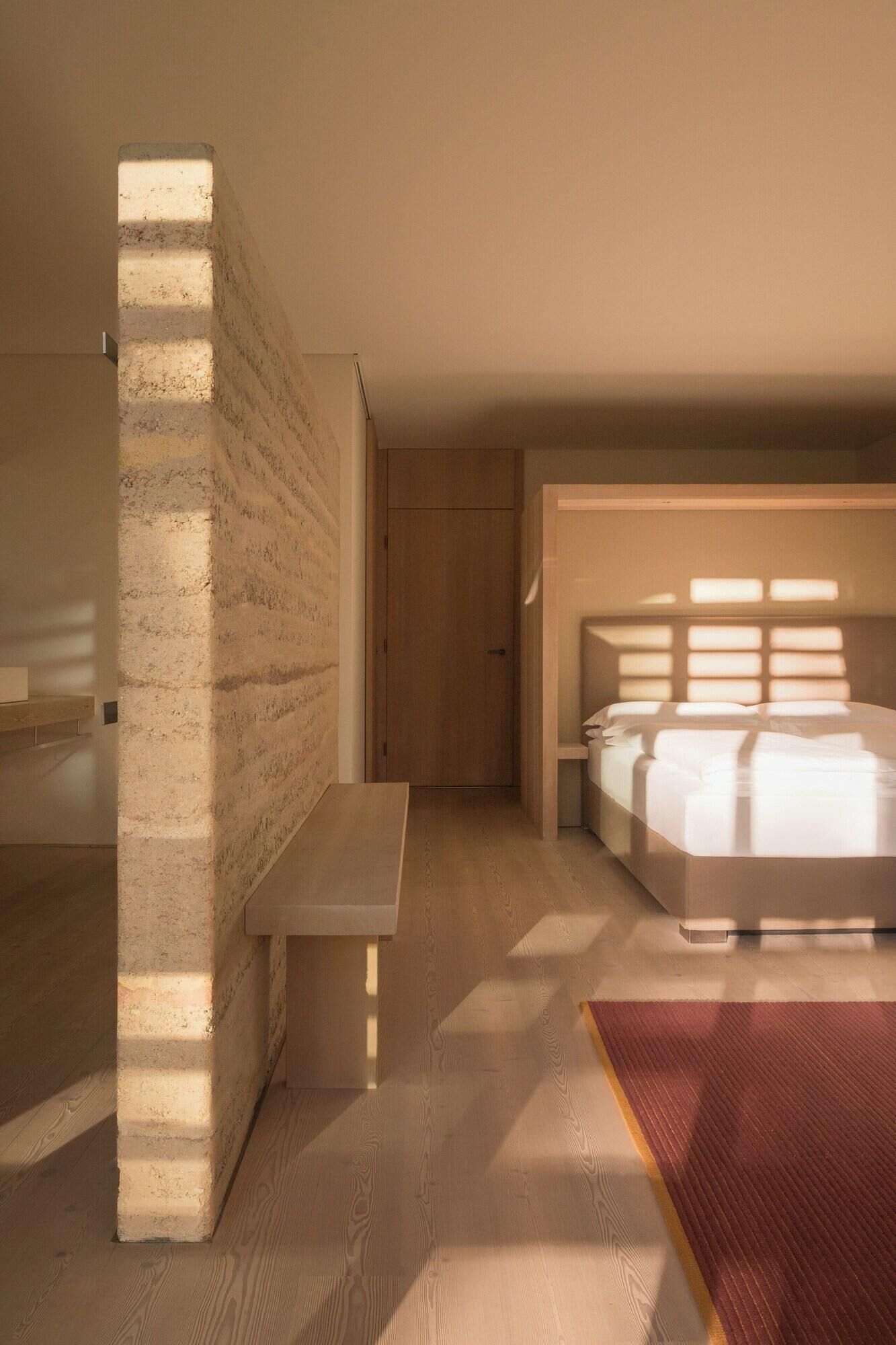 Quarto com cama, um banco e uma porta.