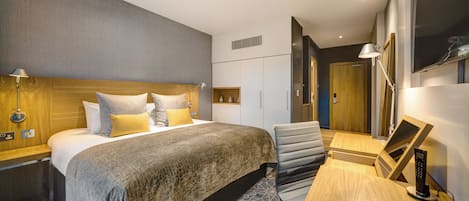 Habitación de hotel con cama, lámparas de noche, escritorio, silla, televisor y puerta.