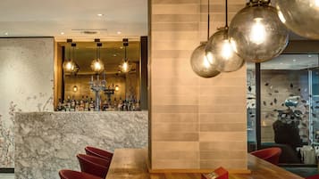 Un espace bar doté d’un comptoir en marbre, de nombreuses bouteilles et de luminaires sphériques suspendus.