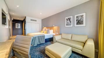 A hotel room with a bed, a sofa, an ottoman, a desk, and a mirror.