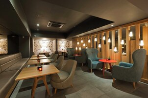 Un interior moderno con arreglos de asientos, mesas y una pared decorativa con patrones geométricos.
