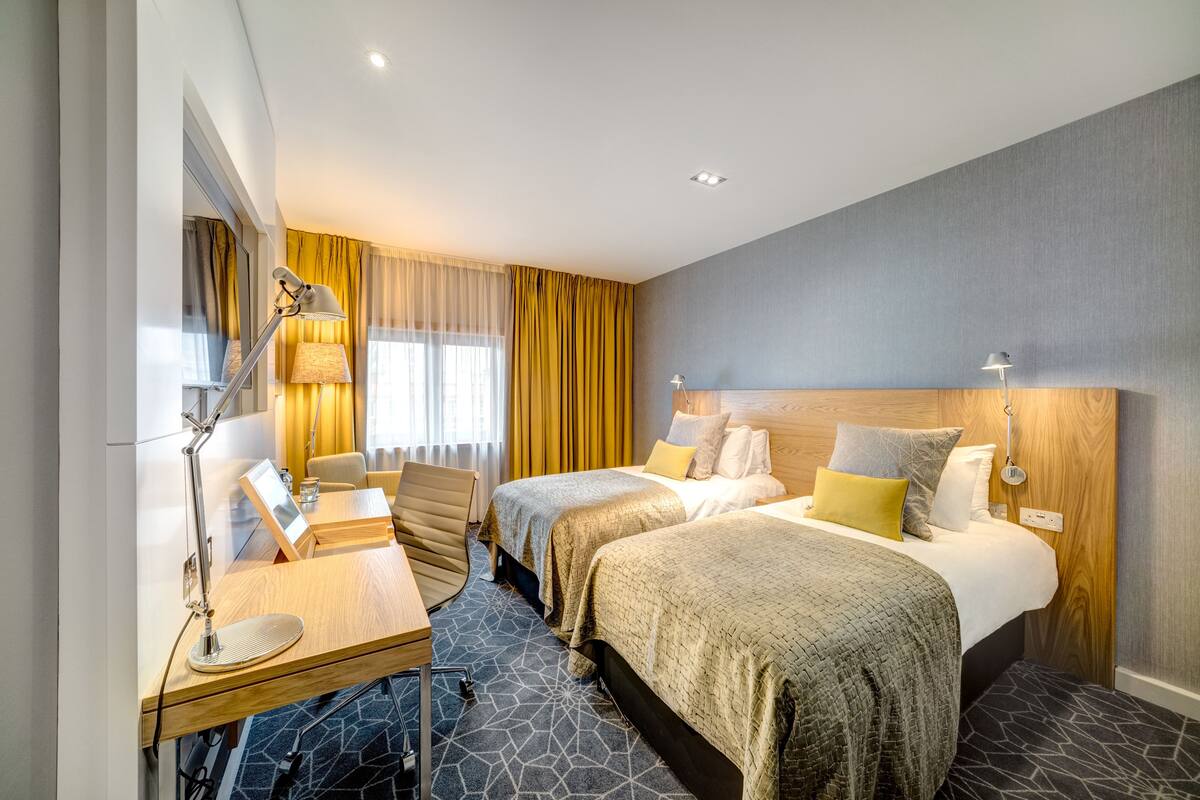 Een hotelkamer met twee bedden, een bureau, een stoel en een lamp.