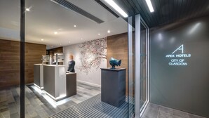 A reception area with a modern design, including a reception desk, a decorative wall, and a logo for Apex Hotels in Glasgow. - Apex City of Glasgow Hotel (Glasgow)