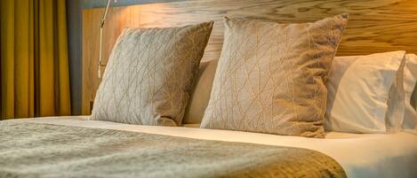 A neatly made bed with a wooden headboard, two patterned pillows, and a bedside lamp.