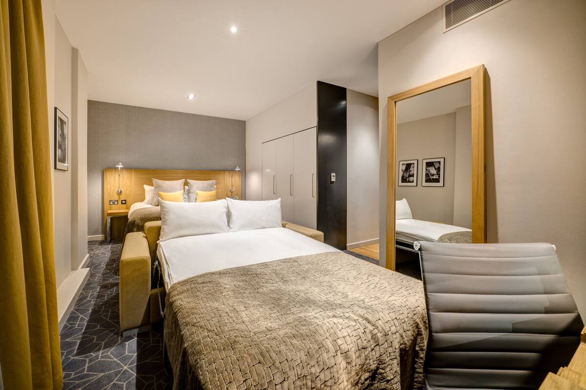 Een hotelkamer met een groot bed, een nachtkastje, een stoel, een spiegel en een garderobe.