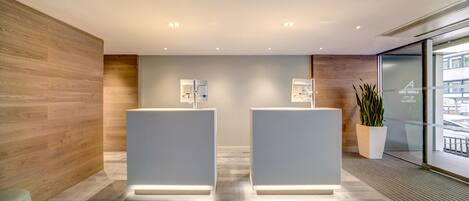 A reception area with two reception desks, a wooden wall, a potted plant, and a glass door leading outside.