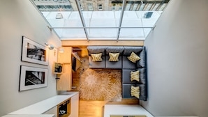 A compact living space with a skylight, a sofa with patterned cushions, a wooden cabinet, and framed pictures on the wall. - Apex City of Glasgow Hotel (Glasgow)