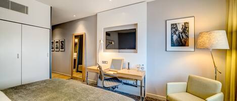 A hotel room with a bed, a desk with a chair, a lamp, a picture on the wall, and a wardrobe.