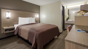 A hotel room with a bed, bedside table, nightstand, and a desk with a mirror.