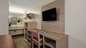 A compact hotel room with a bed, a desk with a chair, a television, and a bathroom with a mirror and sink.