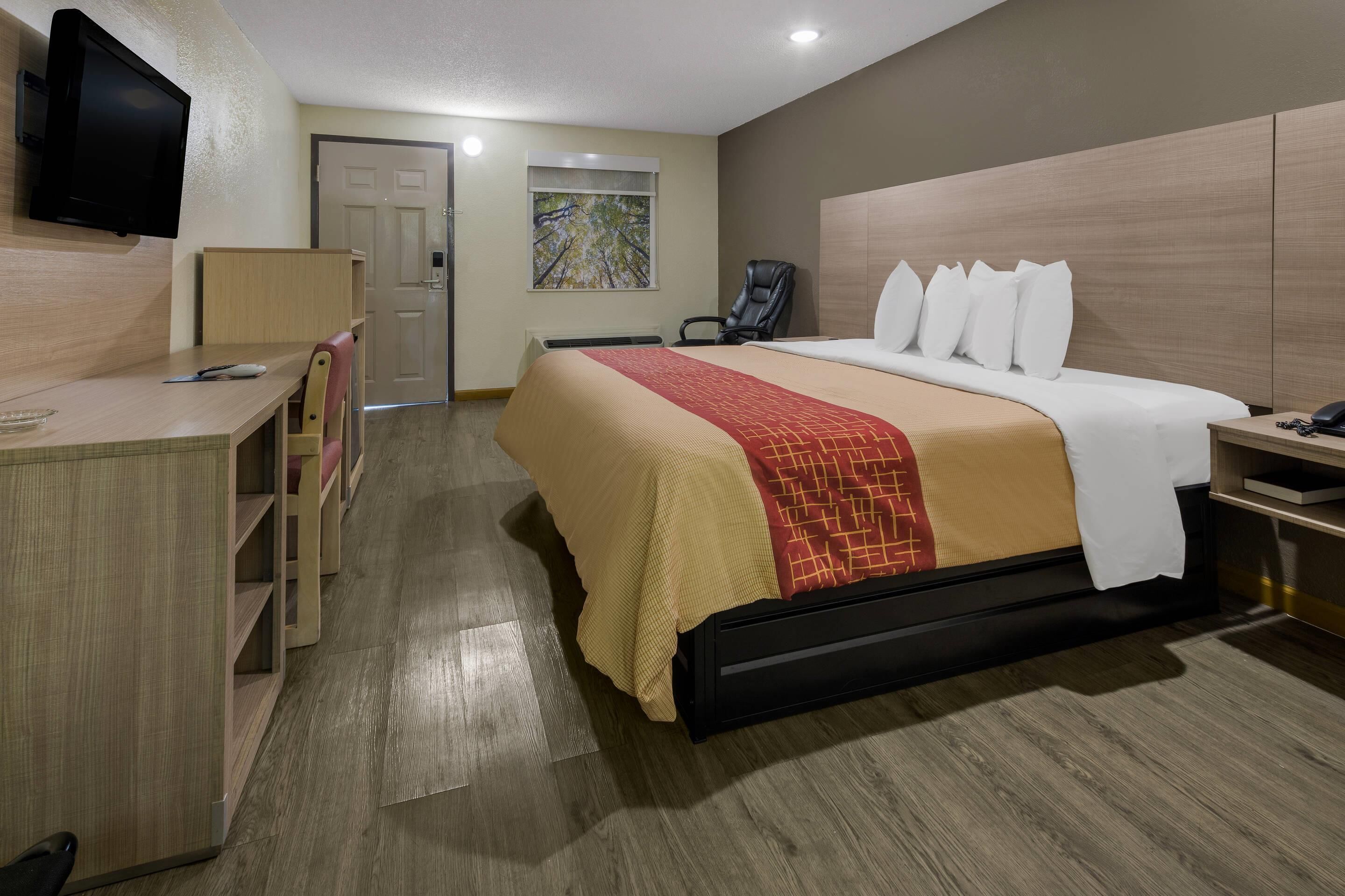 Una habitación de hotel con cama, escritorio, silla, televisor y una obra de arte en la pared.