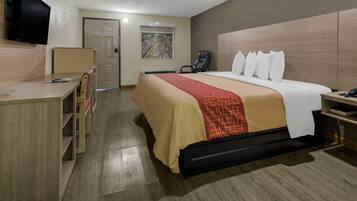 Una habitación de hotel con cama, escritorio, silla, televisor y una obra de arte en la pared.