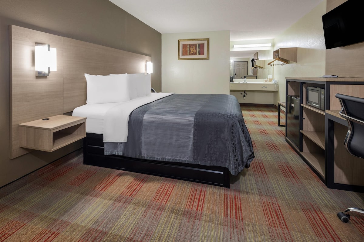 Una habitación de hotel con cama, mesita de noche, escritorio, silla y televisor.