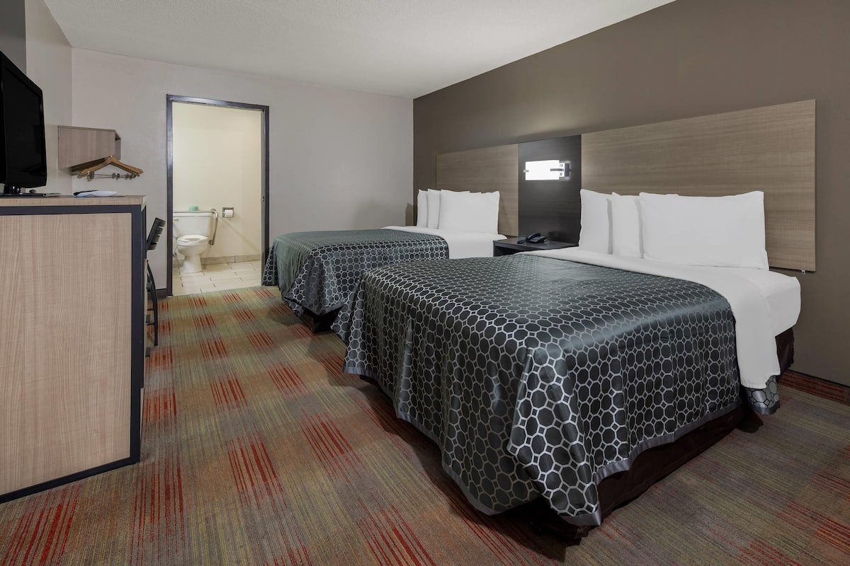 Habitación de hotel con dos camas, un escritorio y televisión, y un baño visible a través de una puerta abierta.