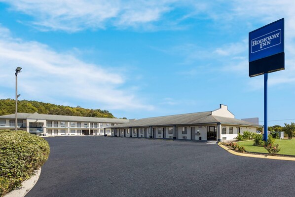 A motel with a large sign, a parking lot, and a building with multiple rooms.
