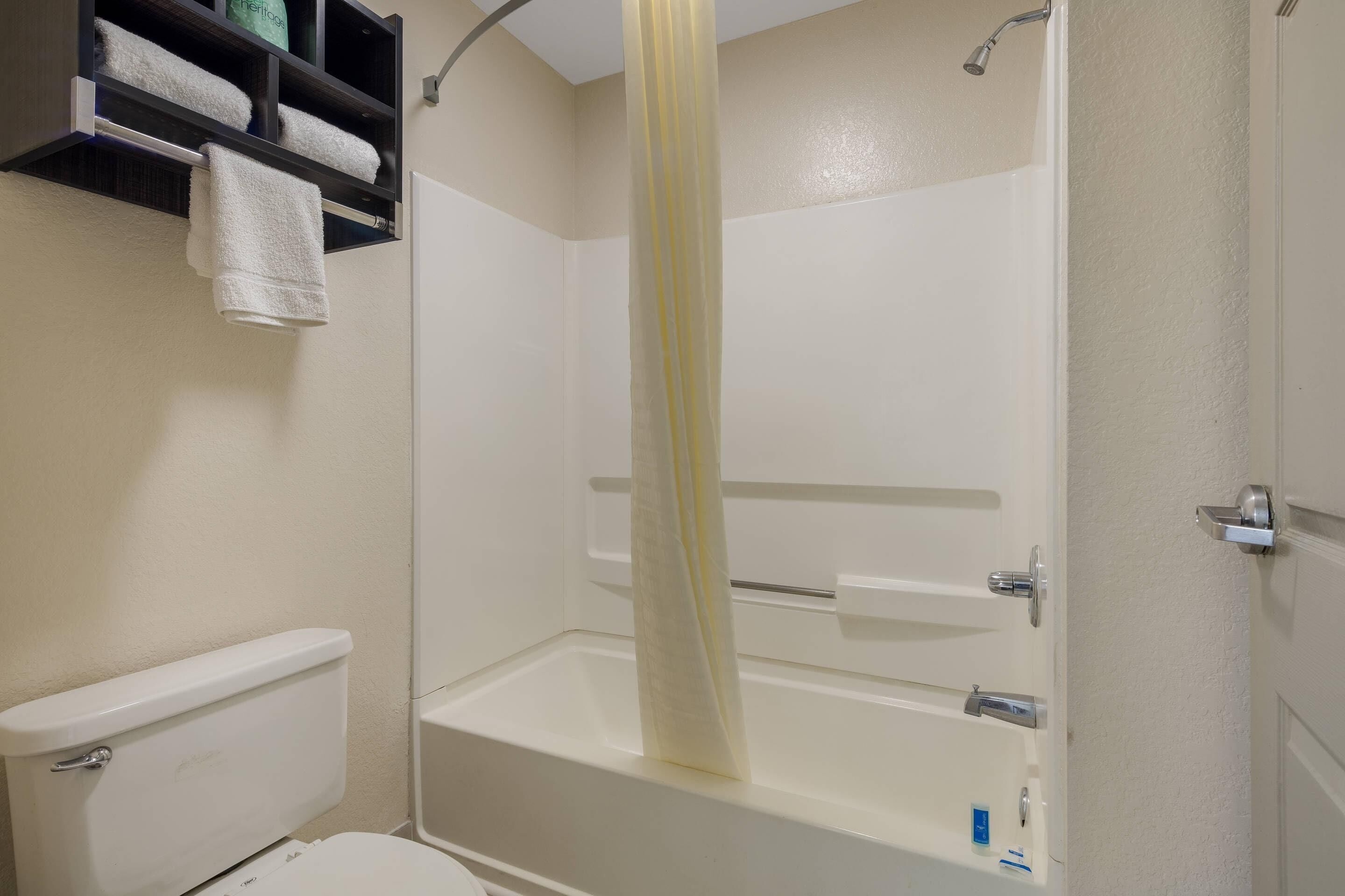 A bathroom with a toilet, a shower with a curtain, and a shelf with towels.