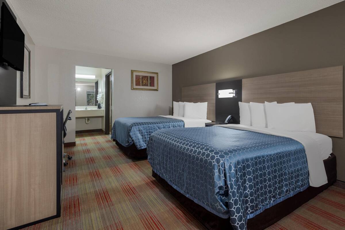 Habitación de hotel con dos camas, un escritorio, un espejo y un cuadro en la pared.