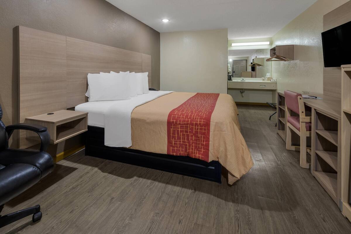 Habitación de hotel con cama, mesita de noche, silla, escritorio y televisor.
