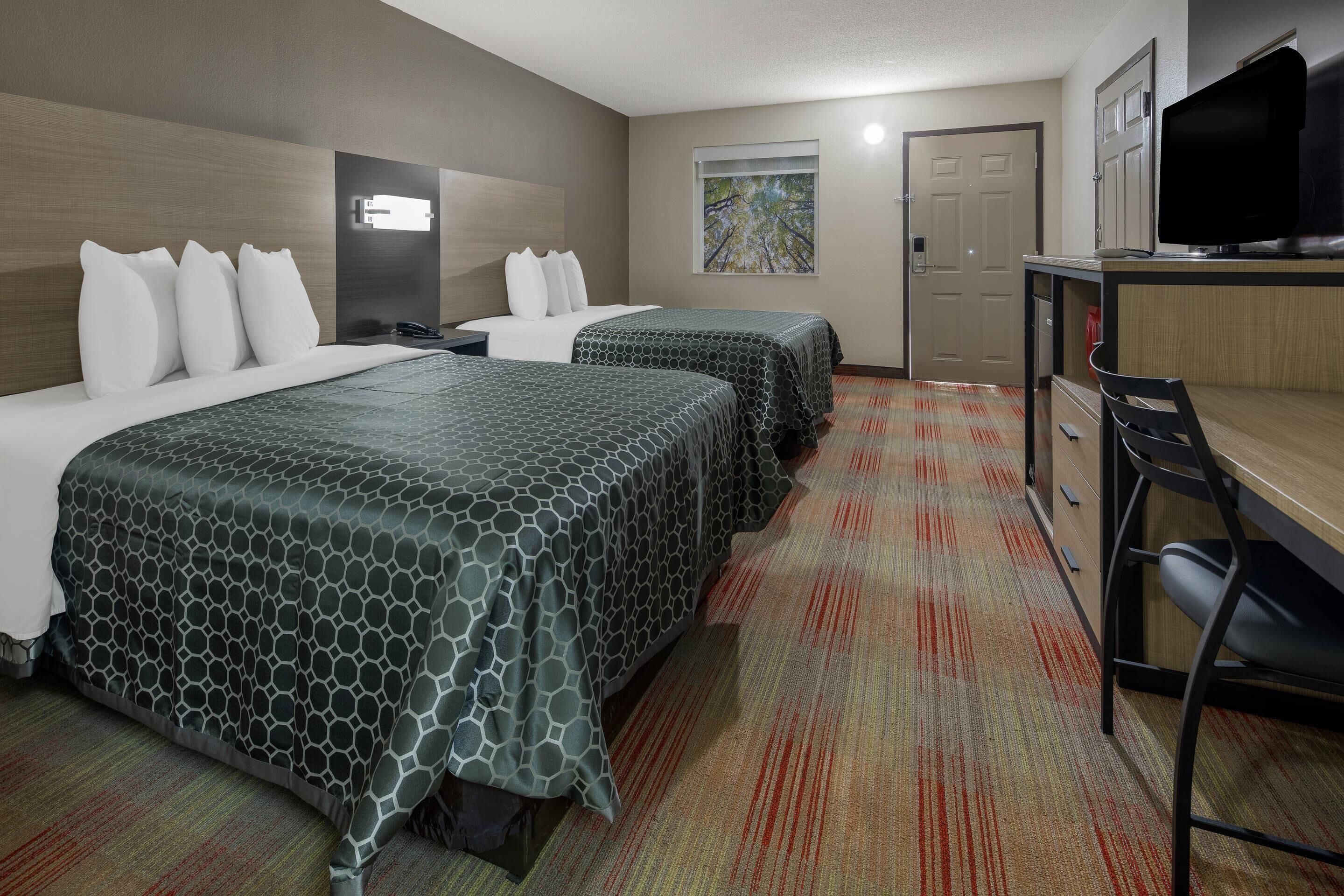 A hotel room with two beds, a desk with a computer, a TV, and a door.