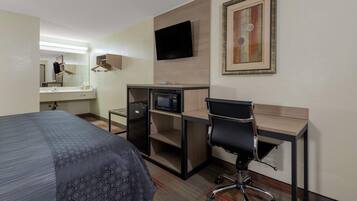 Ett hotellrum med en säng, ett skrivbord, en stol, en TV, en mikrovågsugn och en inramad tavla på väggen.