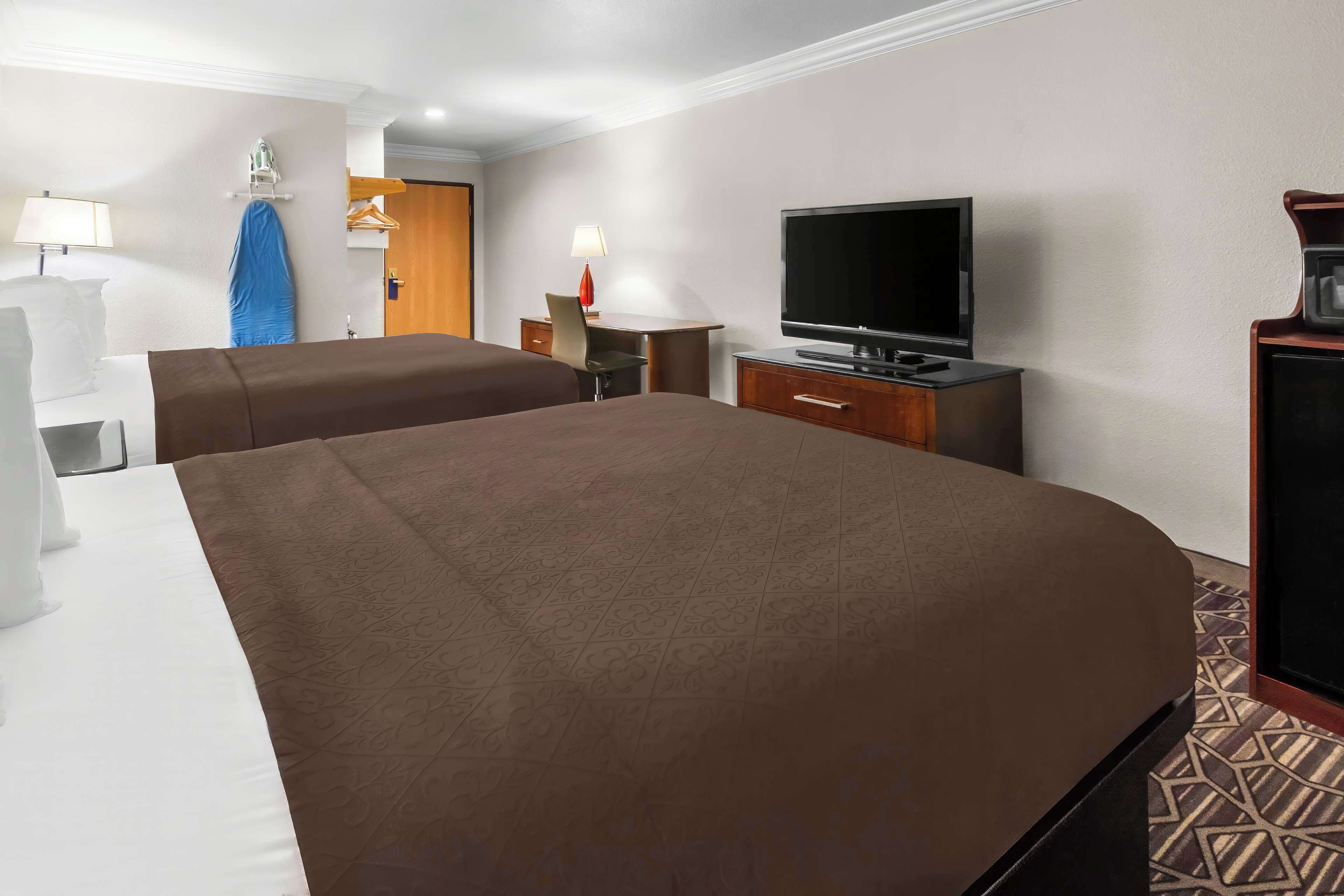 Habitación de hotel con dos camas, televisión, escritorio con lámpara y armario.