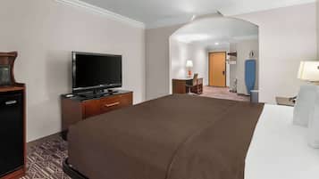 Habitación de hotel con una cama grande, televisor de pantalla plana, escritorio con lámpara y un refrigerador pequeño.
