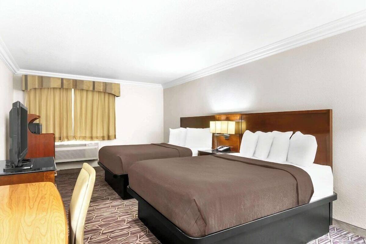 Une chambre d’hôtel avec deux lits, un bureau avec une chaise, une télévision et une fenêtre avec des rideaux.
