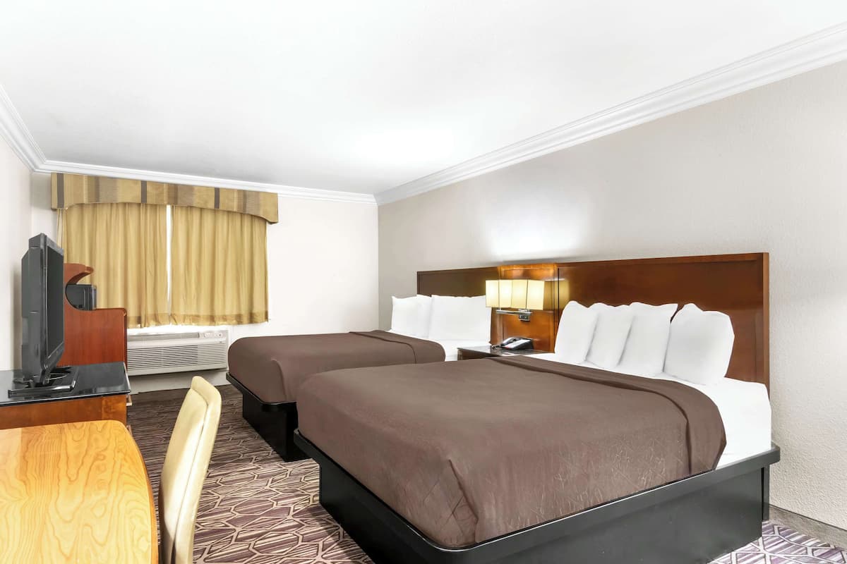 Une chambre d’hôtel avec deux lits, un bureau, une chaise, une télévision et une fenêtre avec des rideaux.