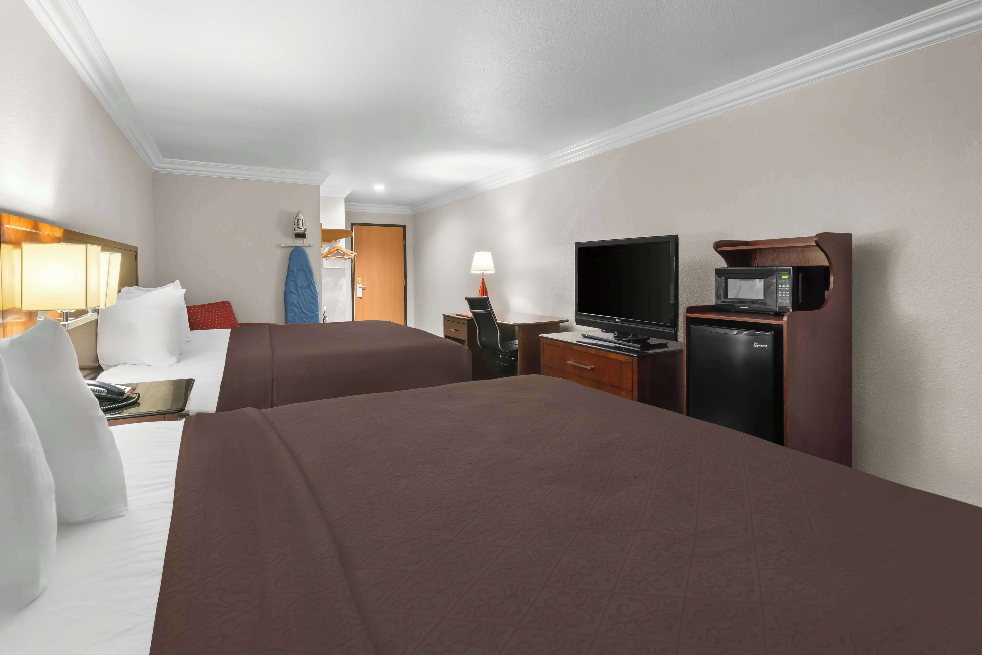 Een hotelkamer met twee bedden, een bureau met een computer, een televisie, een magnetron en een kleine koelkast.