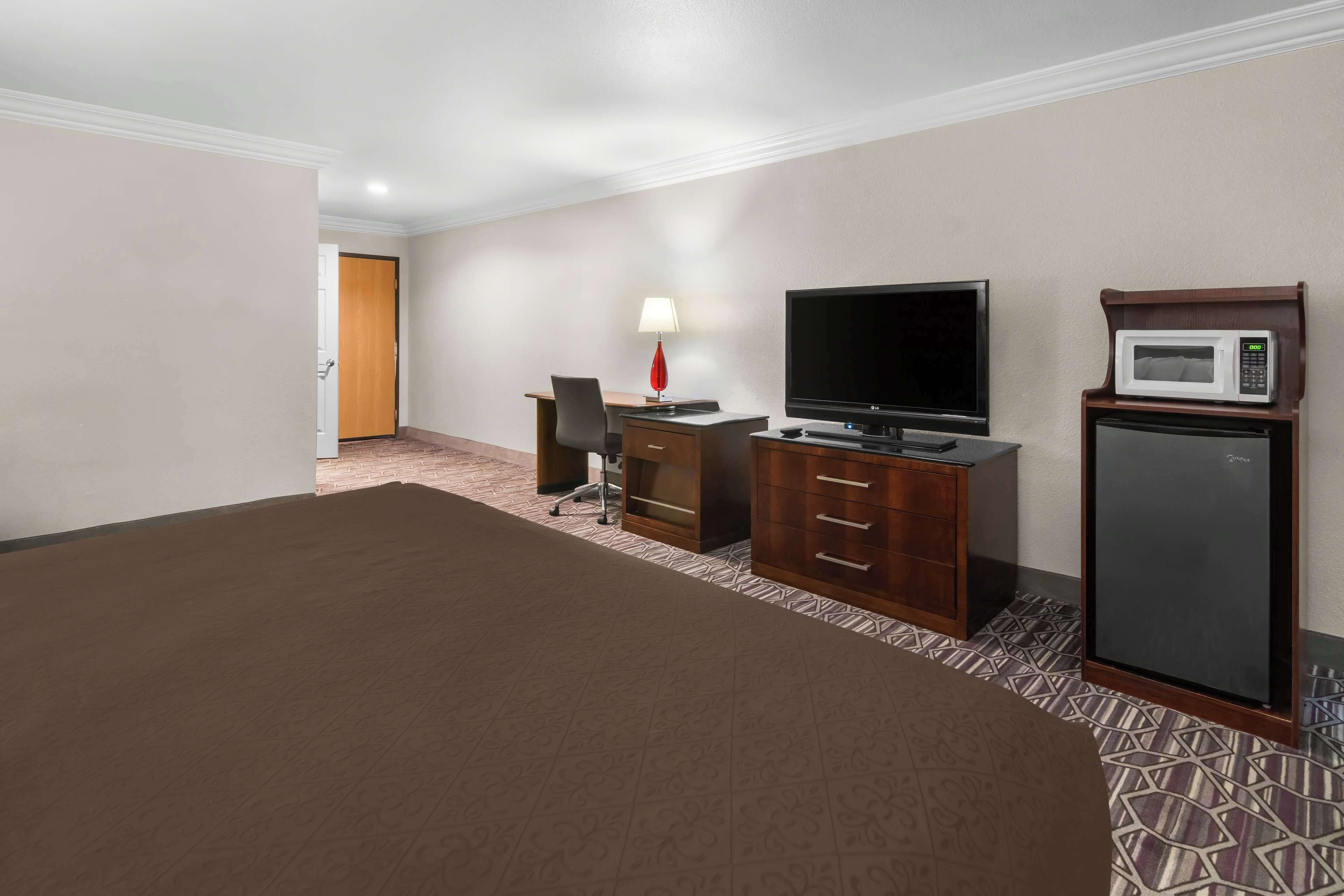 A hotel room with a large bed, a desk with a TV, a lamp, and a microwave.