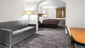 Ein Hotelzimmer mit grauem Sofa, einem Holztisch, einem gemusterten Teppich, einem Bett und einem Schreibtisch mit Lampe.