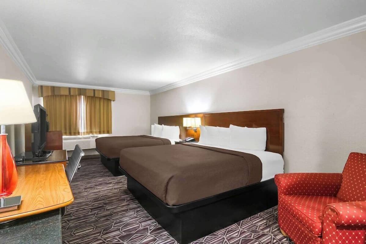 Une chambre d’hôtel avec deux lits, un bureau avec une lampe, une télévision et un fauteuil rouge.